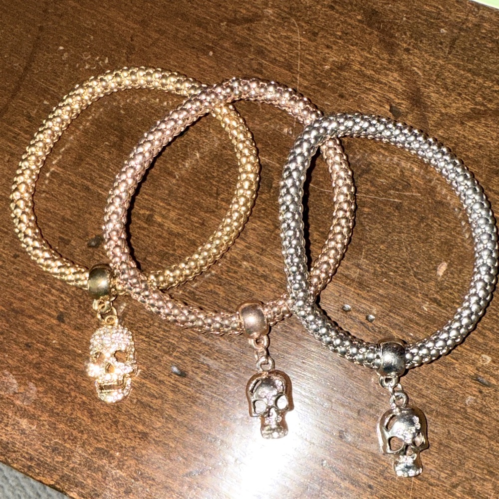 Three Woven Stretch Bracelets in Gold, Rose Gold, and Silver with Skull Charms